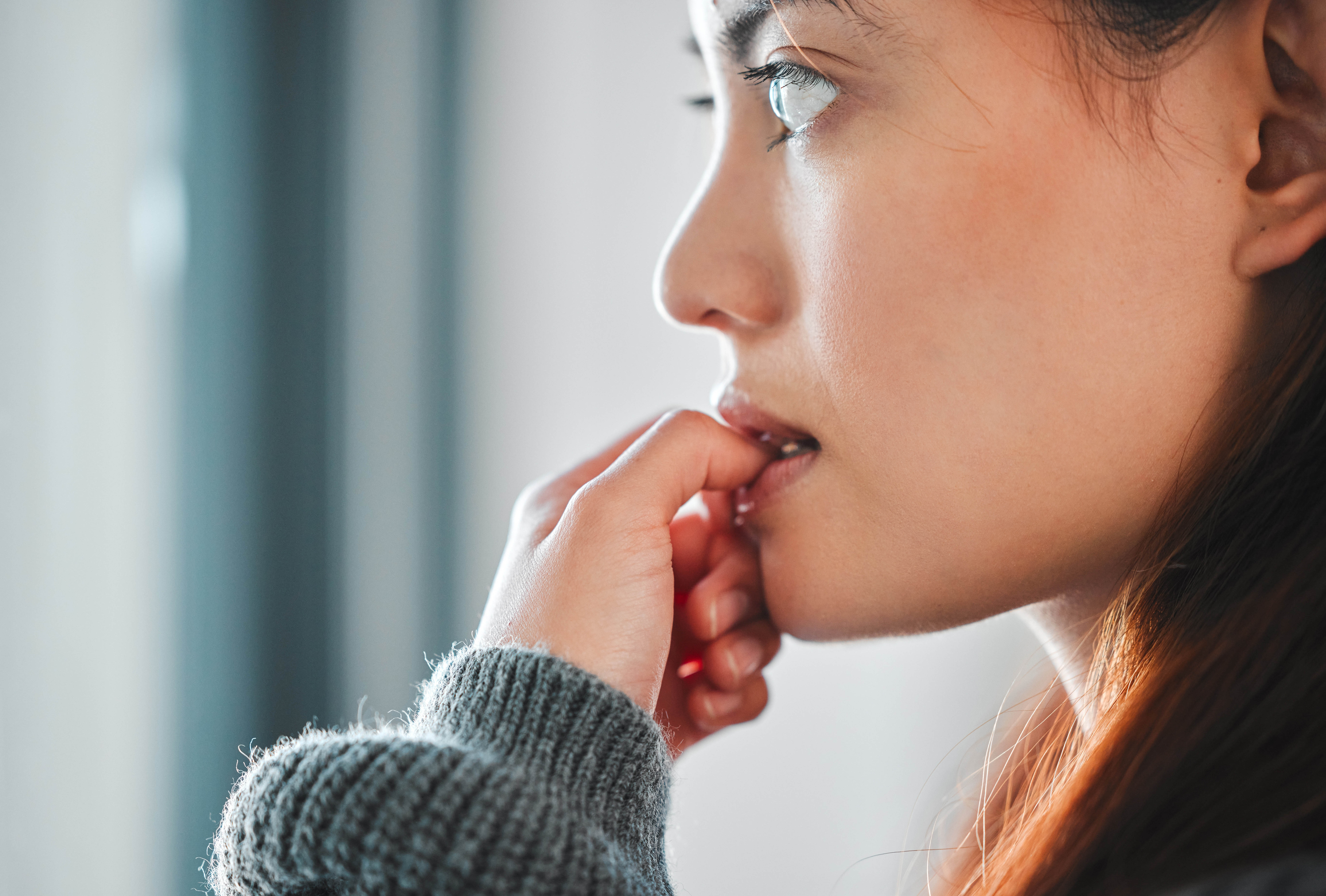 Close-up of woman biting her nails out of anxiety, while looking out the window Close-up of woman biting her nails out of anxiety, while looking out the window